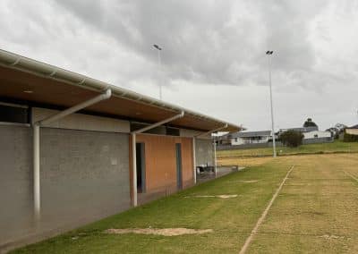 Overcast sky above a single-story building with a covered walkway and tall light poles in a grassy field.