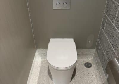 Toilet with a dual-flush panel on a gray wall in a small restroom, tiled walls on the right and a speckled floor