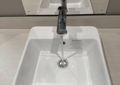 White rectangular sink with a tall chrome faucet on a light countertop; mirror and neutral cabinets visible in the background.