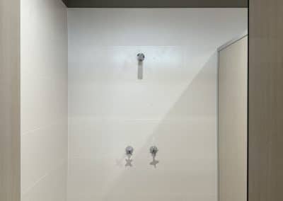 Shower alcove with white tile walls, two chrome water controls, and a central outlet under a dark ceiling edge.