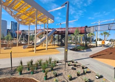 Outdoor playground with twisting metal slides beneath a yellow canopy on a brown mulch surface under a bright blue sky.