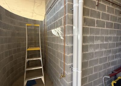 Utility corner with exposed pipes and a yellow step ladder against a gray cinder block wall in an unfinished space