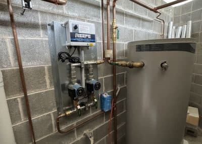 Basement boiler room with copper pipes, a control panel, valves, and a tall cylindrical water heater.