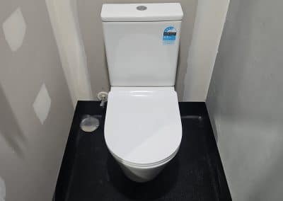 White modern toilet in a narrow gray-walled bathroom with a black speckled floor, viewed from above.