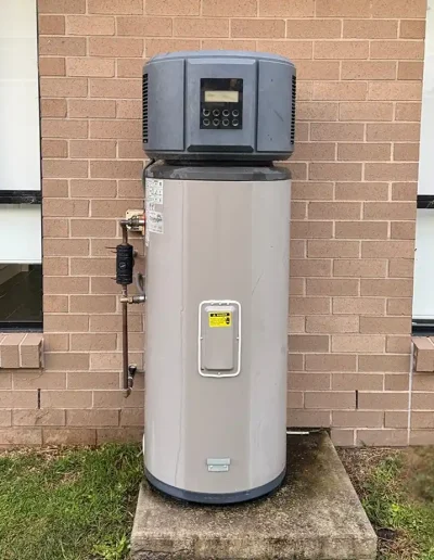 Outdoor electric water heater with control panel on top, mounted against a brick wall.